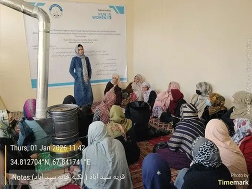 A trainer addresses a group of women seated on the floor of a community room in Bamyan.