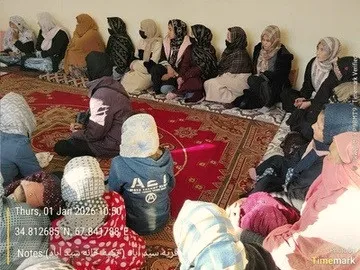 Participants seated on a red carpet in a community hall.