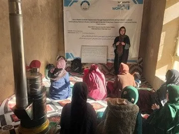 A facilitator speaks beside a stove in a village training room.